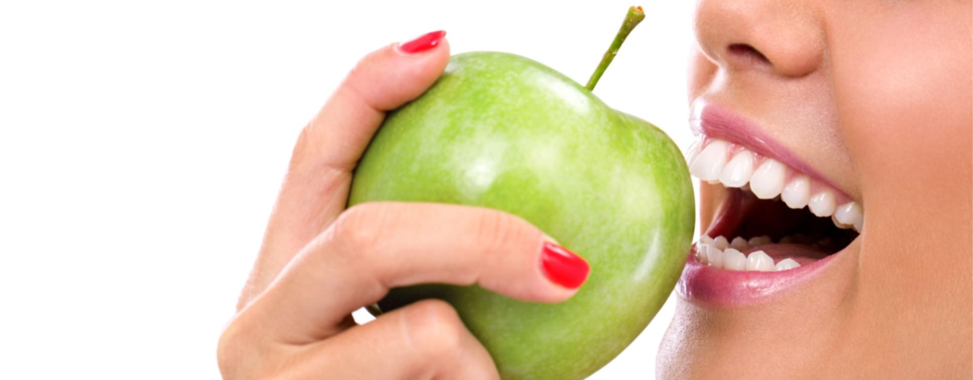 Osoba z białymi zębami je zielone jabłko
